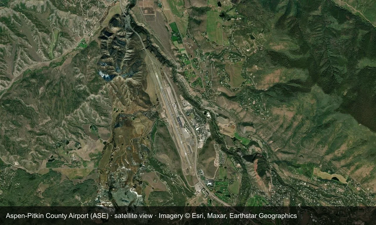 Satellitenansicht: Aspens Startbahn liegt in einem Tal der Rocky Mountains, mit Terminal und Vorfeld daneben und Wald und schneebedeckten Gipfeln ringsum.
