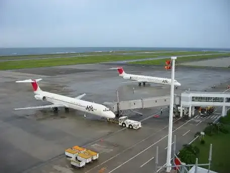 Japan-Air-Commuter-Flugzeuge an den Abstellpositionen – zwei Regionalflugzeuge beim Boarding unter den Schildern, das Meer direkt hinter der Startbahn.