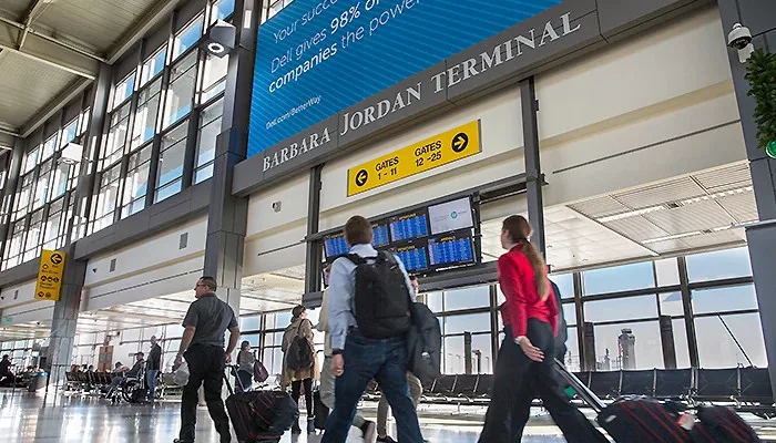 Im Barbara-Jordan-Terminal — Reisende mit Taschen gehen am Schild „C Gates 1–25“ und den Abfluganzeigen vorbei.