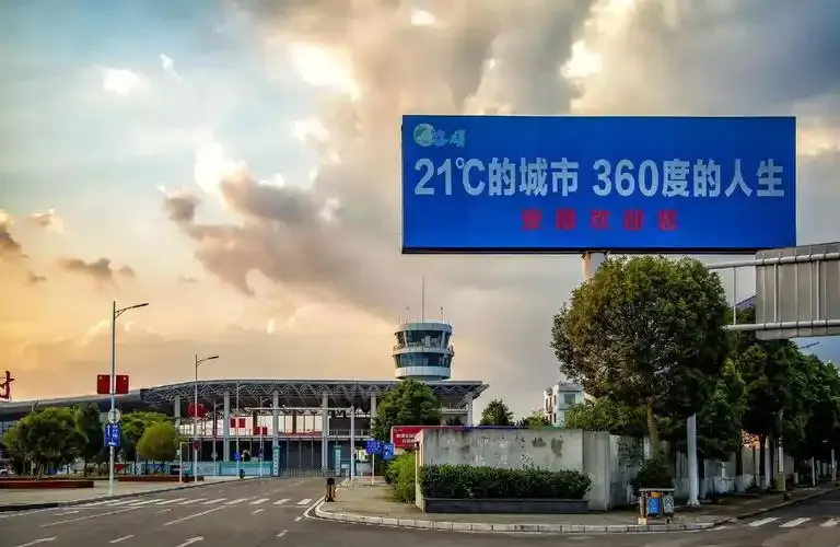 Terminal und Turm in der Dämmerung – eine Plakatwand am Straßenrand mit der Aufschrift „21℃的城市“, der Kontrollturm beleuchtet vor dem Abendhimmel.
