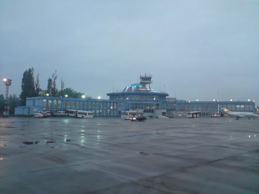 Băneasa in der Dämmerung — das blaue Terminal und der Turm beleuchtet, Busse und ein Verkehrsflugzeug auf dem Vorfeld.