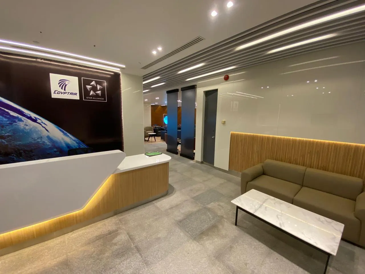 Der Empfang der EgyptAir-/Star-Alliance-Lounge am Flughafen Kairo – Holzvertäfelung und ein Marmor-Couchtisch, ruhige Sitzplätze hinter den Türen (Ägyptisches Ministerium für Zivilluftfahrt, Januar 2025, über den State Information Service).