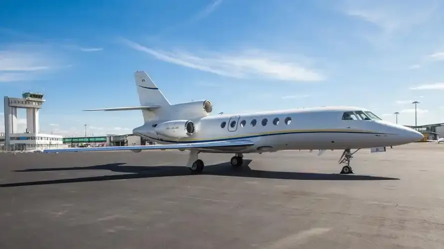 Ein Business Jet von Dassault Falcon auf dem Vorfeld, dahinter Kontrollturm und Terminal.