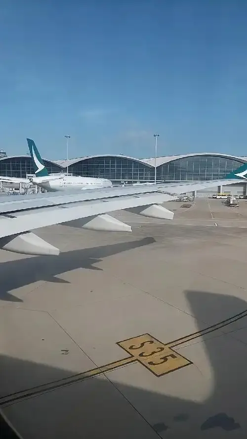 Aus dem Kabinenfenster: ein Flugzeug von Cathay am Stand vor dem gewölbten Dach des Terminals, darunter die Markierung „S35“ auf dem Vorfeld.