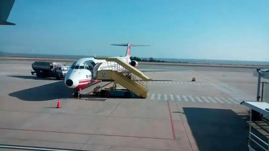 On Kinmen Airport's apron, passengers board an airliner by mobile stairs with ground vehicles alongside.