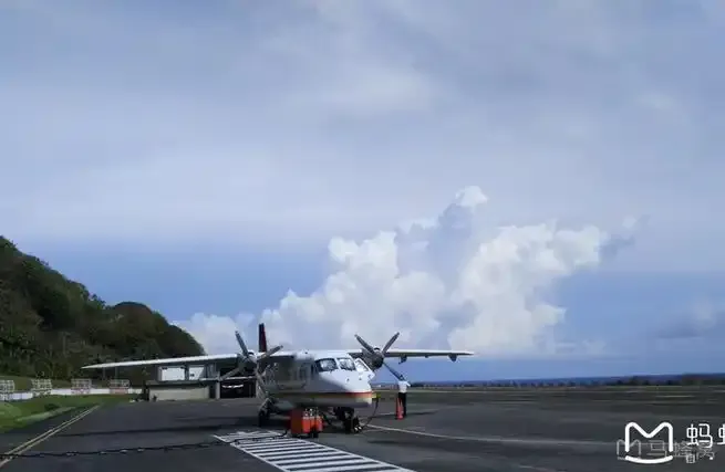 A twin-engine turboprop on Lanyu Airport's apron, with a green hillside and the sea behind it.