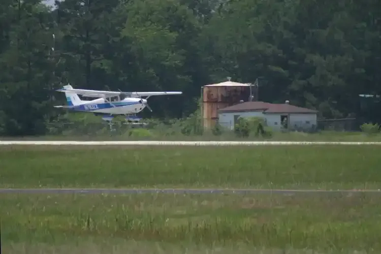 Eine Cessna im Endanflug – die Graspiste und ein rostroter Wasserturm unter ihrer Tragfläche, der ländliche Charakter des Platzes in einem Bild.