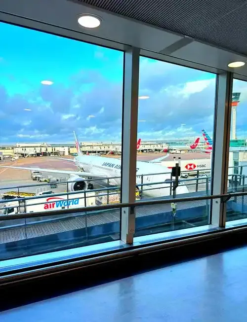 Aus einem Terminalfenster: ein Flugzeug von Japan Airlines am Gate, dahinter der Kontrollturm von Heathrow.