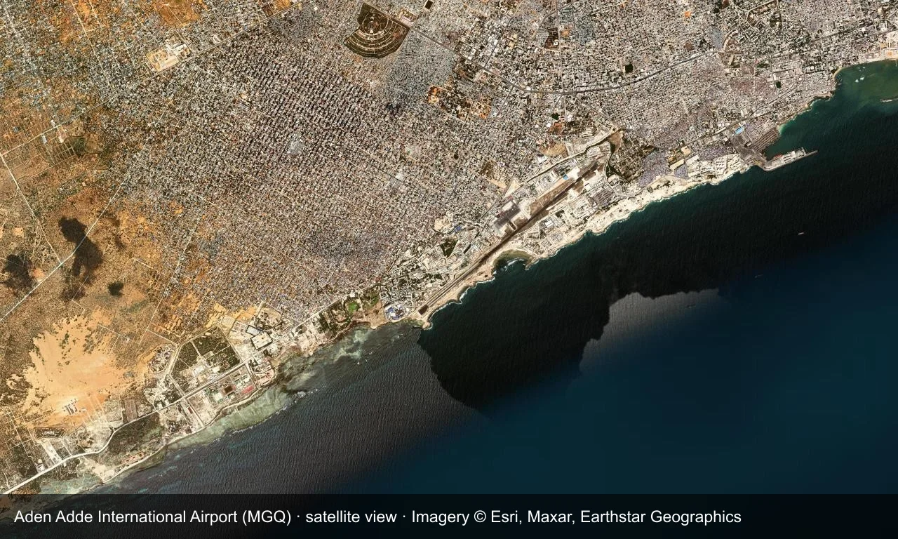 Satellitenansicht: Die Startbahn von Mogadishu liegt an der Küste des Indischen Ozeans, Terminal und Vorfeld daneben, ringsum Stadt und Strand.