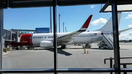 Eine 737 von Norwegian am Gate, durch die Terminalverglasung gesehen, das Bodenpersonal arbeitet um sie herum.
