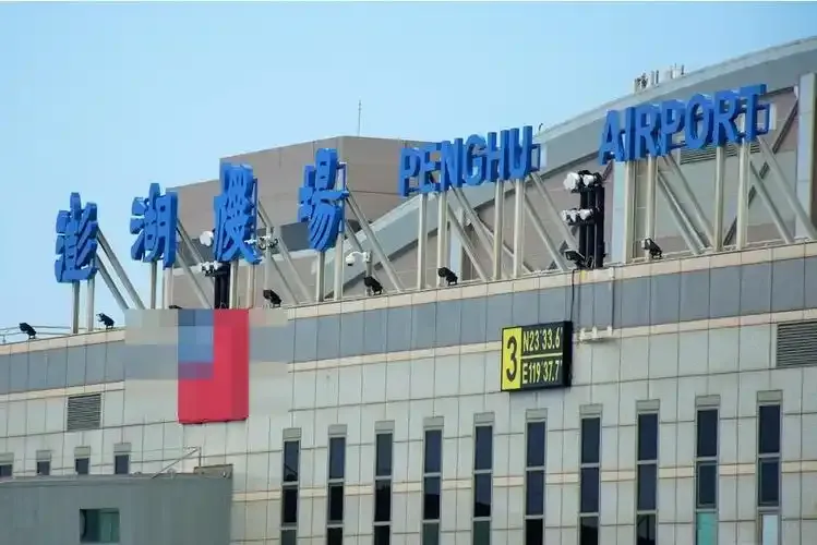 Blue 'Penghu Airport' lettering atop the terminal, beside a sign giving the airport's coordinates.
