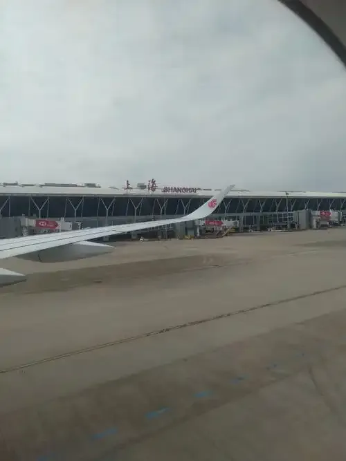 Pudongs Terminal aus einem Kabinenfenster – „上海 SHANGHAI“ auf der Dachkante, Flugzeuge von China Eastern an den Gates.