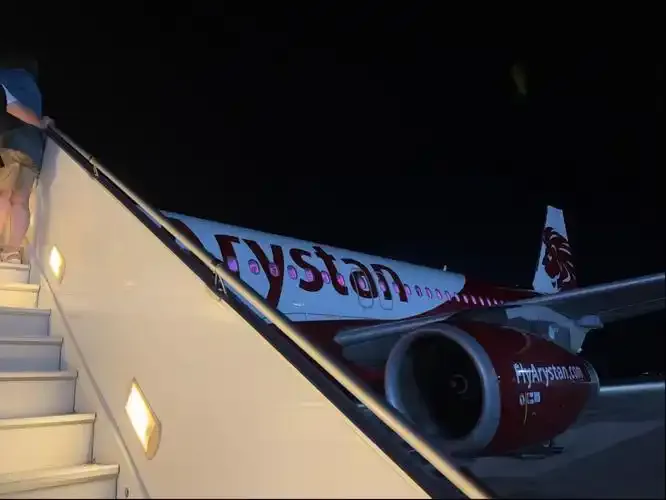 Boarding bei Nacht – Passagiere steigen die Treppe zu einer Maschine von FlyArystan hinauf, deren rotes Farbschema unter dem Vorfeldlicht scharf hervortritt.