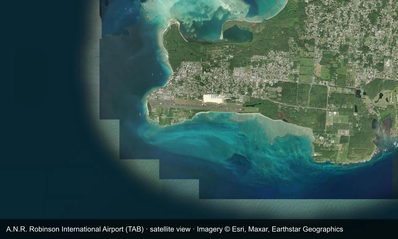 Satellitenansicht: Die Startbahn von Scarborough liegt neben der Küste von Tobago, Terminal und Vorfeld daneben, Strand und grüne Hügel ringsum.