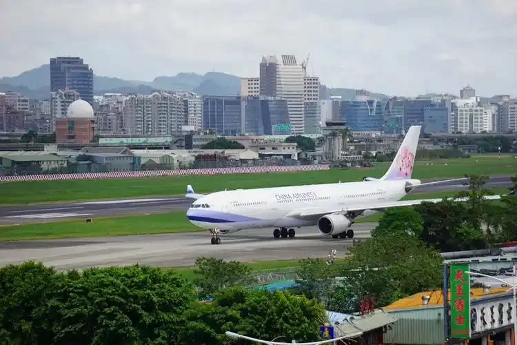 A China Airlines jet rolls along Songshan's runway with Taipei's skyline rising behind it.