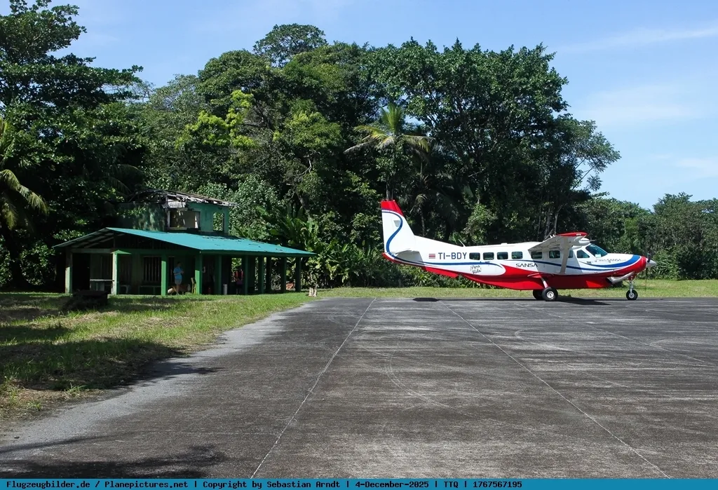Der Flugplatz Tortuguero – eine Cessna Caravan von Nature Air (TI-BDY) auf dem Asphalt, der kleine Warteschuppen mit grünem Dach und der Regenwald direkt hinter dem Flügel (Foto: Sebastian Arndt / Flugzeugbilder.de).